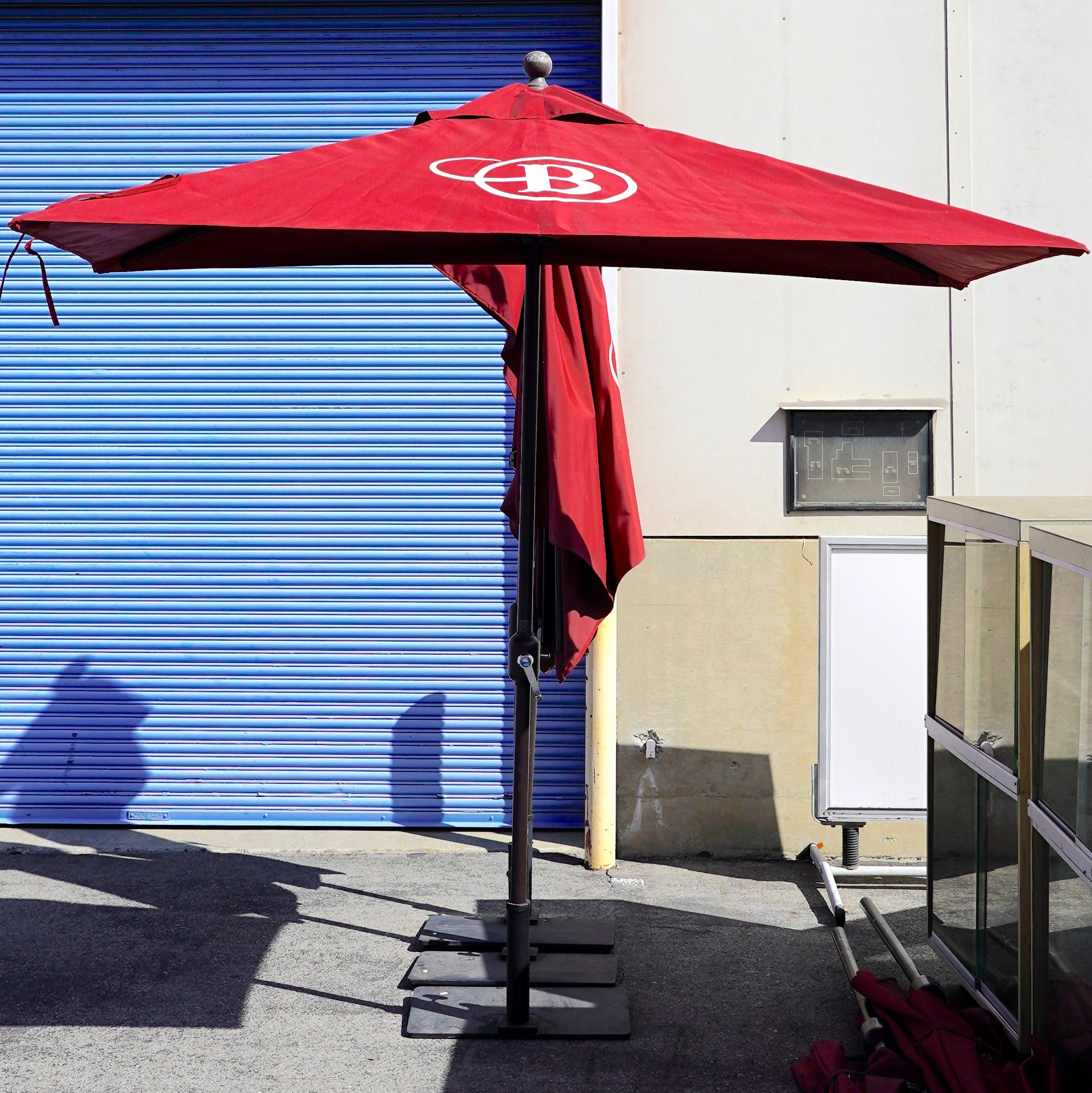 Outdoor red half umbrella with a dark brown metal base.