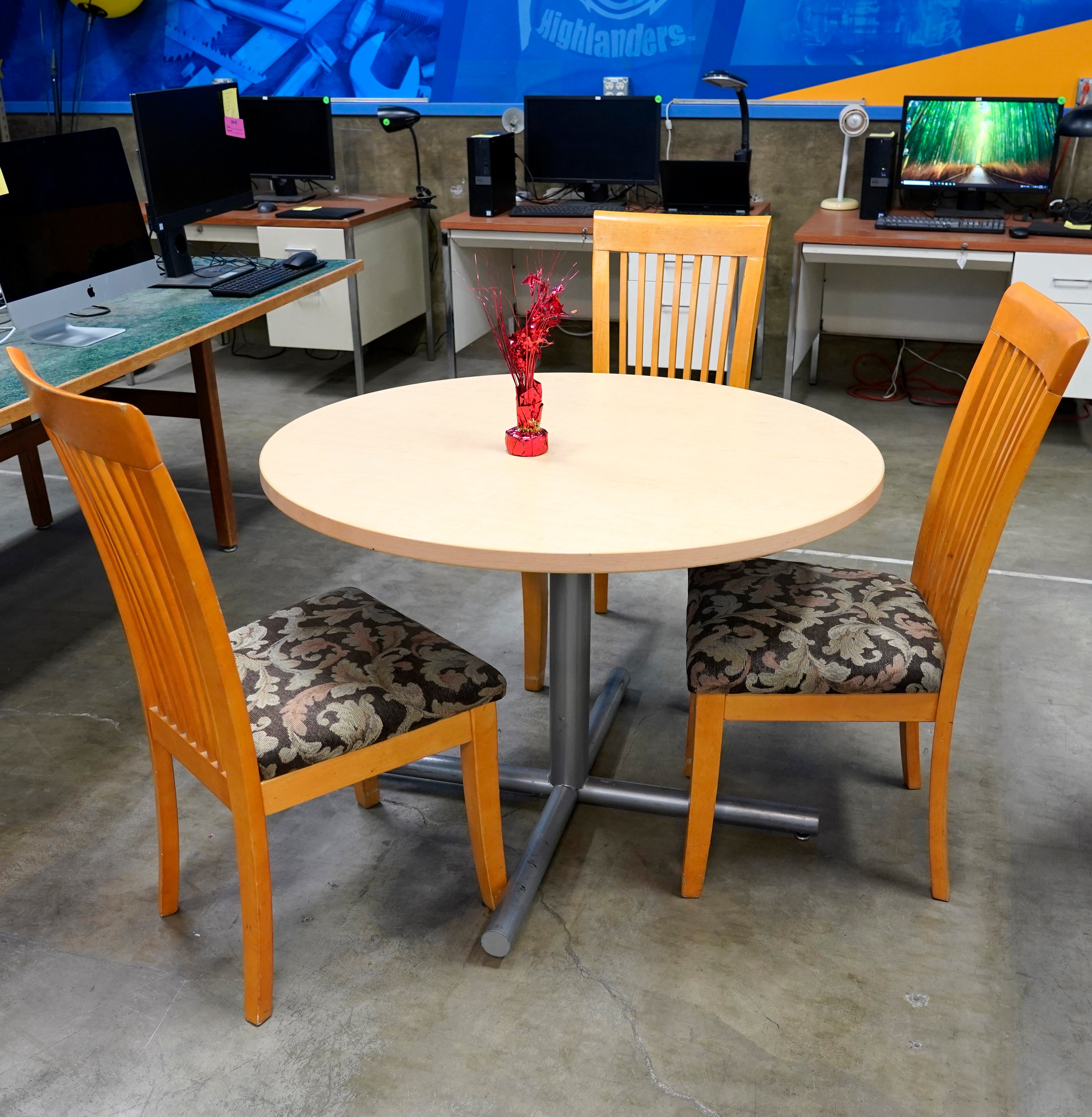Light wood round table with 3 wood chairs that have black cushions.
