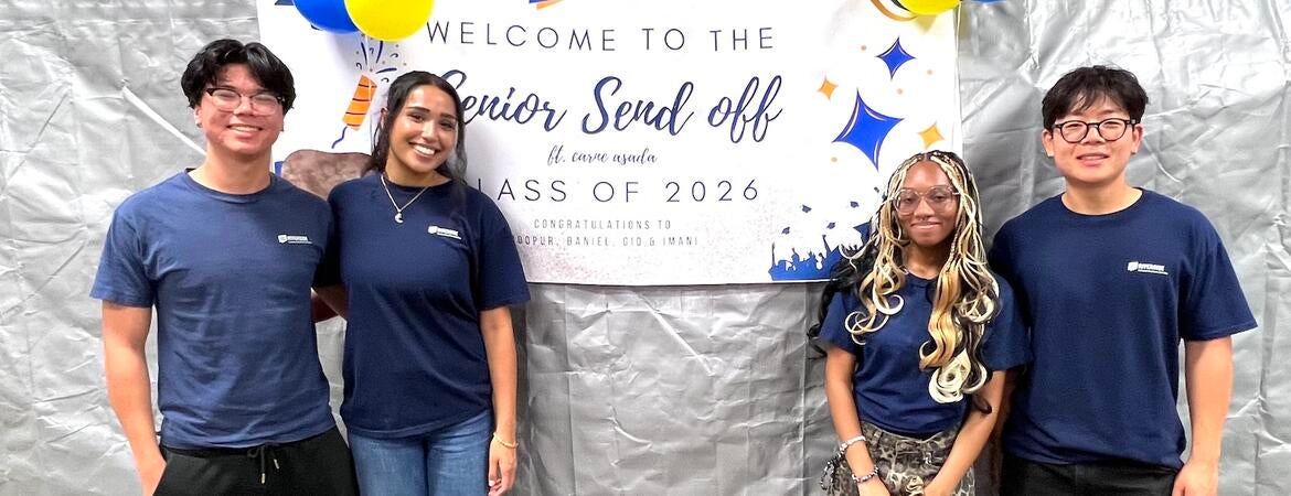 Four graduating CBS student workers pose in front of a "Senior Send Off" banner.