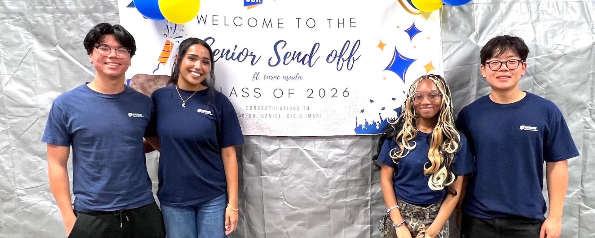 Four graduating CBS student workers pose in front of a "Senior Send Off" banner.